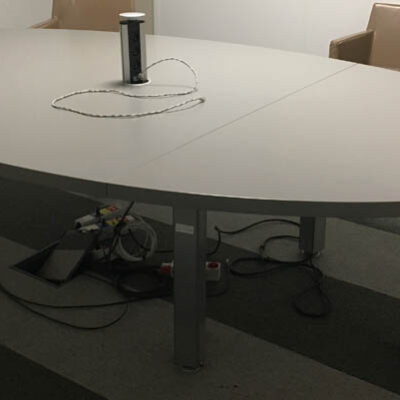 Table de réunion de forme ovale en 3 plateaux en bois stratifé gris avec trappe technique comprenant 3 prises électriques et 2 prises Rj45, reposant sur 6 pieds en acier. 74 x 290 x 170 cm.