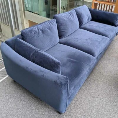 Canapé 3/4 places de marque MADE.COM recouvert de velours bleu, coussins amovibles, pieds en acier laqué noir. 60 x 220 x 95 cm. Localisation : 2 ème coursive