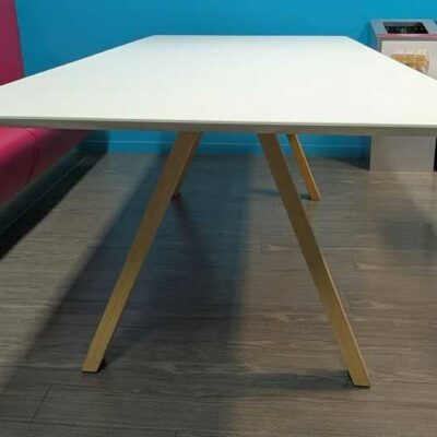 Table rectangulaire, plateau en bois stratifié blanc reposant sur 4 pieds obliques en bois naturel. 73 x 240 x 100 cm. Localisation : 4 est