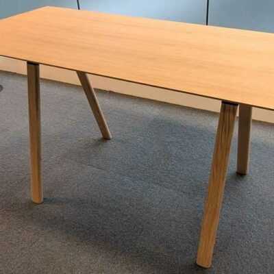 Table haute en bois couleur chêne clair, plateau rectangulaire reposant sur 4 pieds obliques. 104 x 200 x 90 cm. Localisation : 6 est