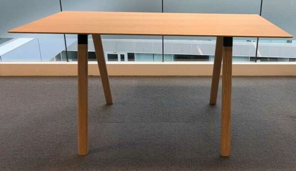 Table haute en bois couleur chêne clair plateau rectangulaire reposant sur 4 pieds obliques. 104 x 200 x 90 cm. Localisation : 6 passerelle