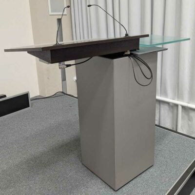 Pupitre de marque WALTER KNOLL à 2 plateaux dont l’un incliné en bois type wenge avec emplacement pour 2 micros et l’autre en verre. Socle ouvrant par une porte sur 3 étagères. 110 x 125 x 55 cm. Localisation : 7 est (audit)