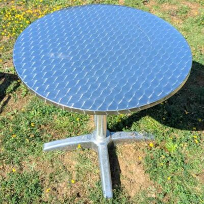 2 tables rondes de marque RODET en aluminium, plateau en bois stratifié revêtu d’inox. 73 x 70 (abimées). Localisation : extérieur