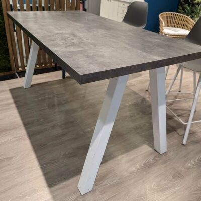 Table haute plateau rectangulaire en bois effet béton, piètement oblique en acier laqué blanc. 90 x 180 x 90 cm. Localisation : Theta 1er cafet