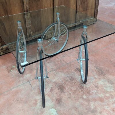 Table montée sur 4 roues de vélo, plateau carré en verre transparent (2 éclats à 2 coins). 74 x 120 x 120 cm. Localisation : 8 rue de la Fossé aux Leux 91700 Ste Geneviève des Bois