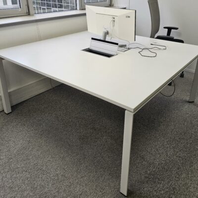 Bureau de type bench de deux postes de travail, plateau blanc et piètement blanc. Equipé de cloisonnette. Dimensions: 160 x 160 cm.. Quantités disponibles 344 unités.