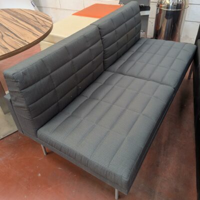 Canapé de marque Geiger modèle Tuxedo recouvert de tissu matelassé gris, piètement en métal. 77 x 142 x 70 cm. Localisation : 8 rue de la Fossé aux Leux 91700 Ste Geneviève des Bois