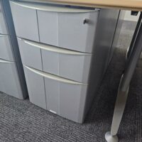 Bureau d'angle en bois couleur miel clair reposant sur un piètement métallique triple en acier gris. Dimensions: 160 x 160 cm. On y joint son caisson à hauteur d'appui. Quantités disponibles: 830 unités. Localisation : 8 av. de Lunca - 78180 Montigny-le-Bretonneux. – Image 3