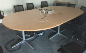 Table de réunion de forme ovale en 3 parties, plateau en bois stratifié couleur hêtre avec trappe technique, piètement en acier laqué gris. 75 x 320 x 180 cm. Localisation : 8 av. de Lunca - 78180 Montigny-le-Bretonneux. (5F02-1)