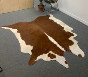 Tapis en peau de vache naturelle, teintes brunes et blanches. 
200 x 100 cm.
Localisation : Rdc