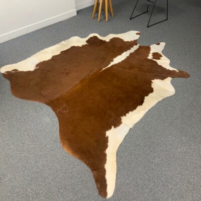 Tapis en peau de vache naturelle, teintes brunes et blanches. 
200 x 100 cm.
Localisation : Rdc