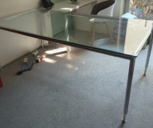 Table ou bureau de marque Bosse modèle Modul Space, plateau rectangulaire en verre transparent reposant sur une structure en acier chromé, pieds réglables en hauteur. 76 x 200 x 100 cm. Localisation : 1-21