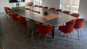 Table de réunion, en bois, avec un plateau en forme de tonneau, trappes techniques et surfaces antidérapantes noires, sur piétements en métal.
72 x 480 x 220 cm.
Localisation : 6 rue Duret - 75116 Paris, 
(RDC haut salle Pékin.)