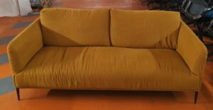 Canapé 4-5 places recouvert de tissu ocre,  dossiers amovibles et déhoussables, piétement en acier laqué noir. 82 x 200 x 60 cm. Localisation : 5 avenue Kleber - 75116 Paris