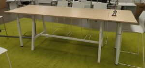 Table rectangulaire ajustable en hauteur de marque Buronomic, plateau couleur hêtre sur un piètement en acier laqué blanc avec entretoise. 105 x 300 x 100 cm. (1er bat A)