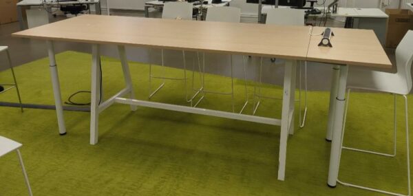 Table rectangulaire ajustable en hauteur de marque Buronomic, plateau couleur hêtre sur un piètement en acier laqué blanc avec entretoise. 105 x 300 x 100 cm. (1er bat A)