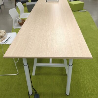 Table rectangulaire ajustable en hauteur de marque Buronomic, plateau couleur hêtre sur un piètement en acier laqué blanc avec entretoise. 105 x 300 x 100 cm. (1er bat A)