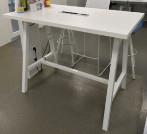 Table haute rectangulaire, plateau en bois stratifié blanc avec trappe technique électrique, piètement oblique en acier laqué blanc avec entretoise. 105 x 140 x 80 cm. (1er bat A)
